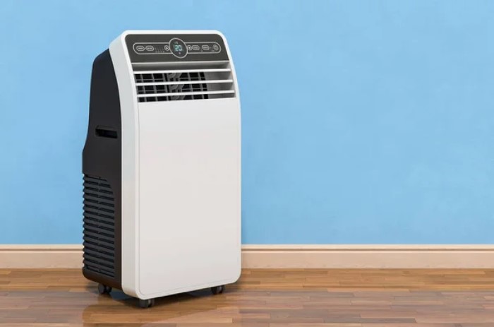 Aparelho de ar condicionado portátil branco e preto, virado de frente, próximo a uma parede azul clara. O piso é de madeira, cor marrom. Imagem representando o melhor ar condicionado portátil.