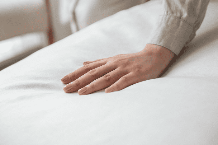 Mulher passando a mão em um colchão macio com lençol branco.