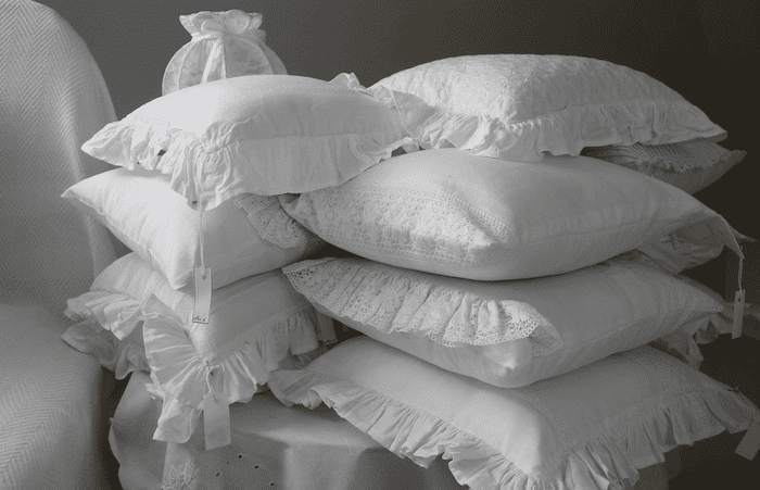 Vários travesseiros brancos bordados empilhados em uma bancada coberta com lençol branco.