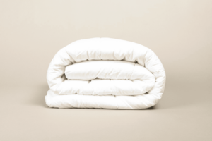Pillow top branco macio, dobrado em camadas, próximo a uma parede cor bege. O chão é da mesma cor. Imagem representando a diferença entre pillow top e pillow in.