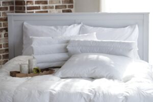 Cama com pillow top branco e 4 travesseiros diferentes brancos, vista de perto.